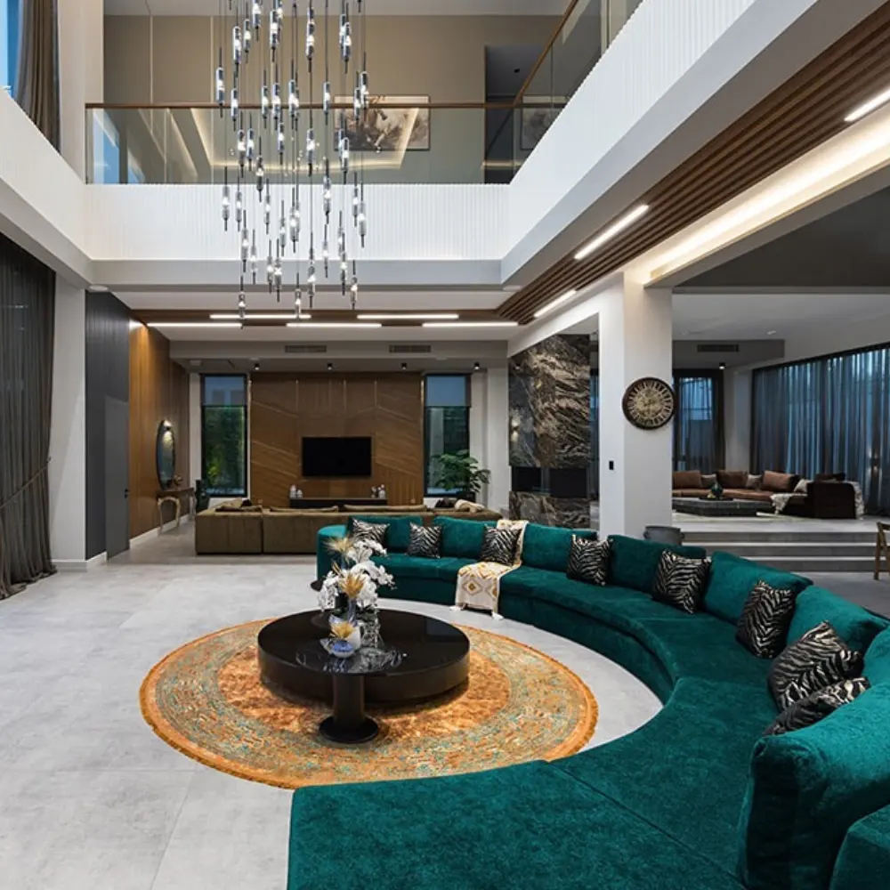 Luxury villa interior design UAE with a curved teal sofa, grand chandelier, and open mezzanine.